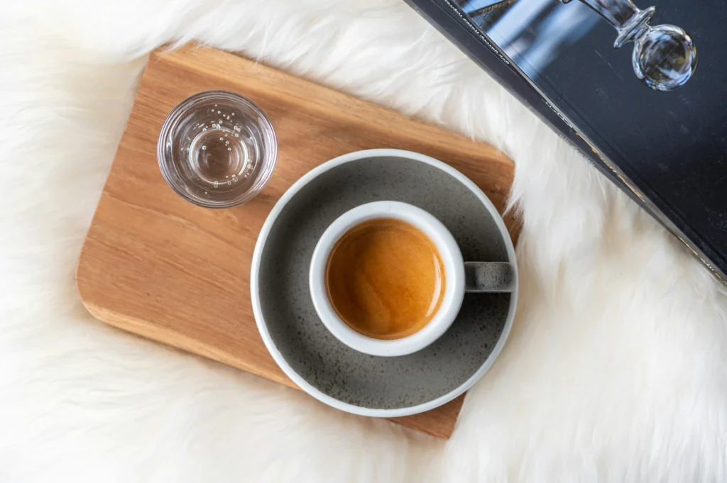 Foto de un espresso recien extraído con una crema perfecta acompañado de un vaso con agua.
